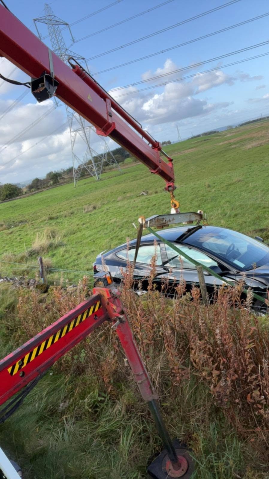 Lorry-loader crane lifting a car from a roadside verge
