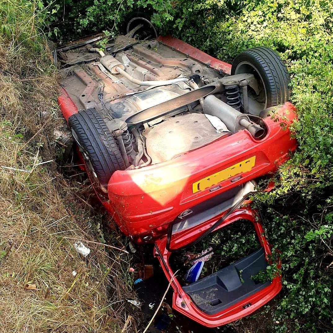 Overturned red car in a roadside ditch awaiting recovery