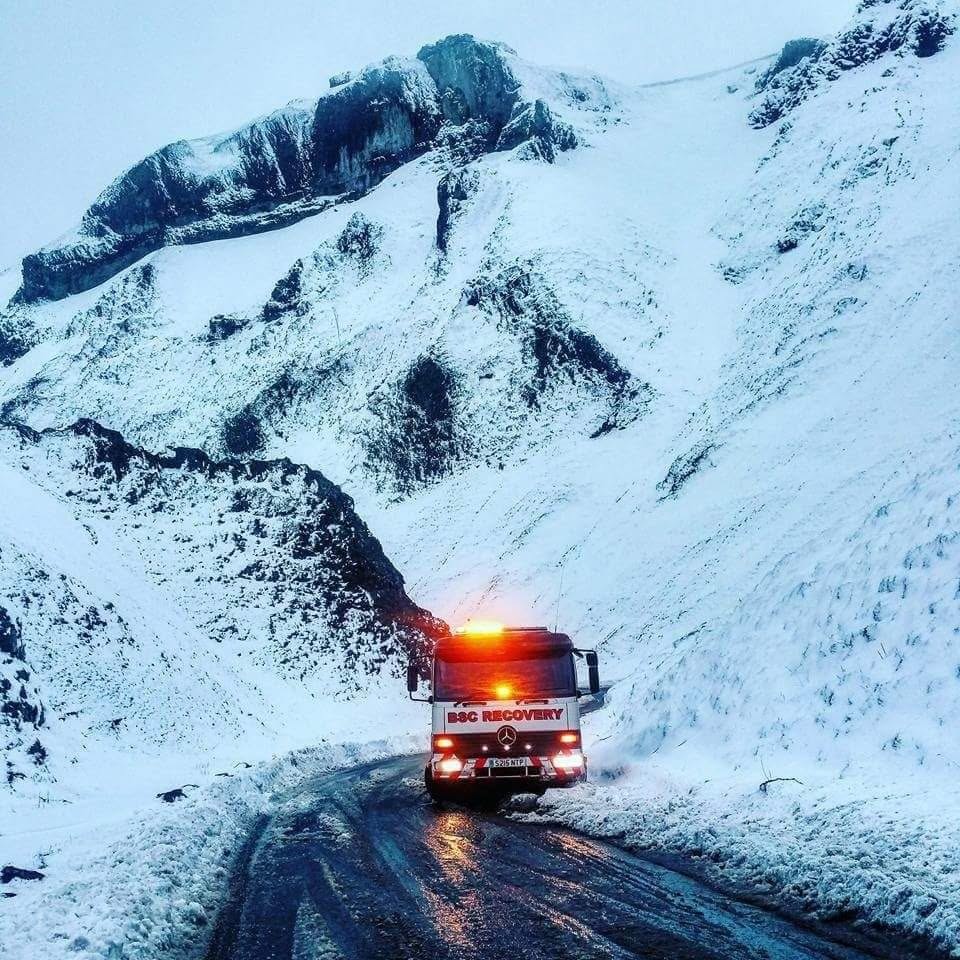 Recovery truck with amber beacons working on a snow-covered road